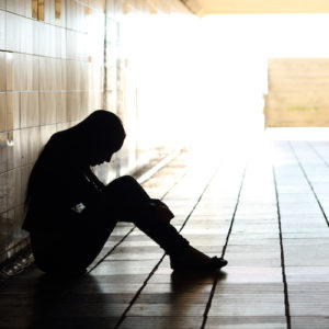 Backlight of a teenager depressed sitting inside a dirty tunnel